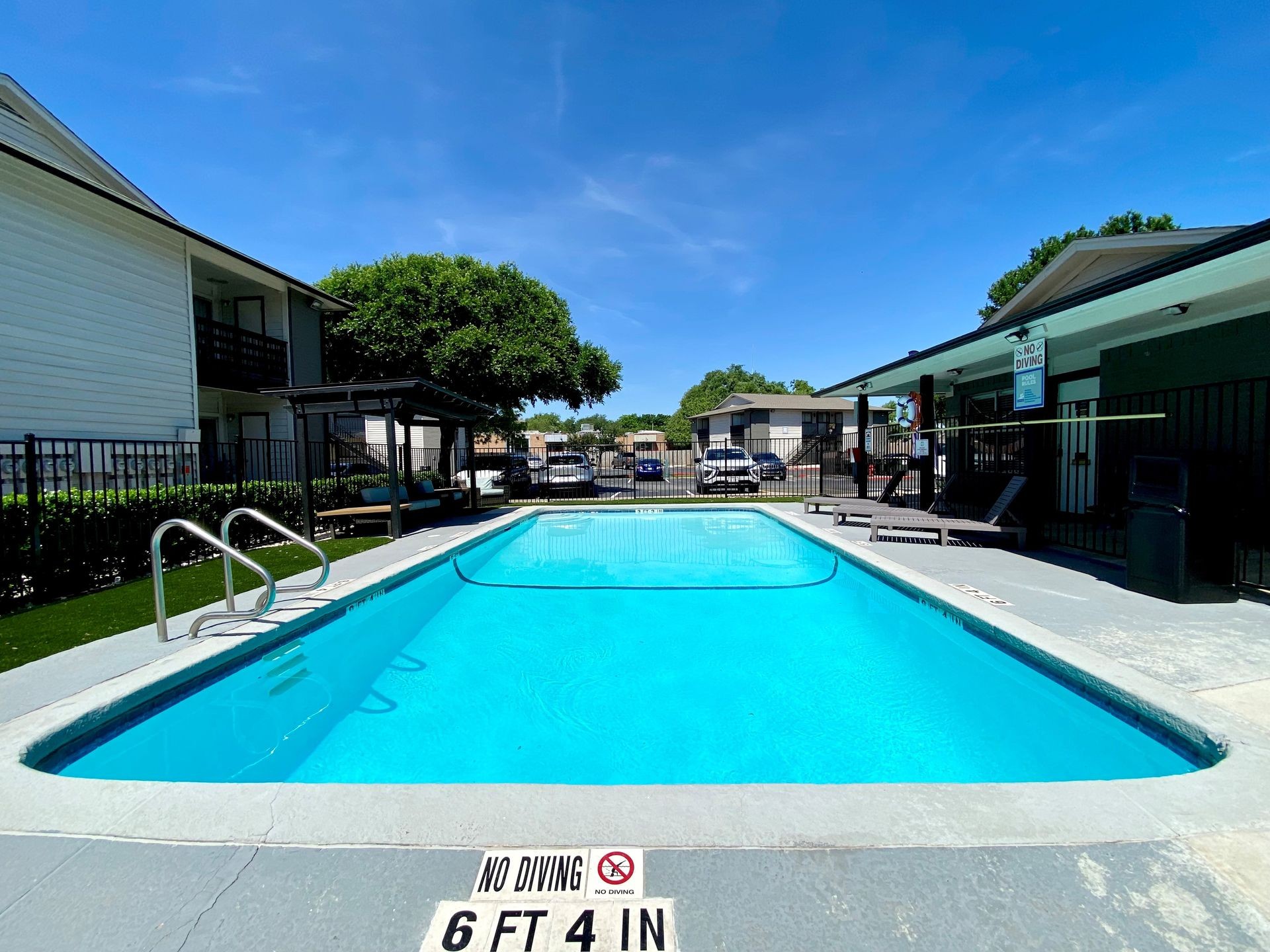 Outdoor swimming pool surrounded by apartment buildings and lounge chairs on a sunny day.